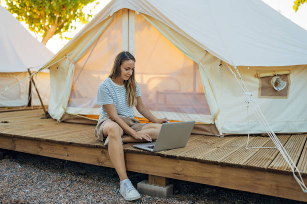 istock Female freelancer sitting in front of glamping tent, using laptop for remote work during vacation 2195722893