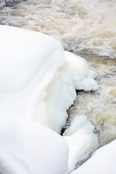 Rushing water flowing through beautiful ice formations along rural river in frozen winter landscape.