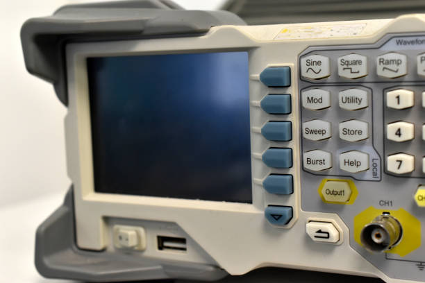 Close-up of a gloved technician adjusting a digital oscilloscope displaying square wave signals during an electrical test or calibration.