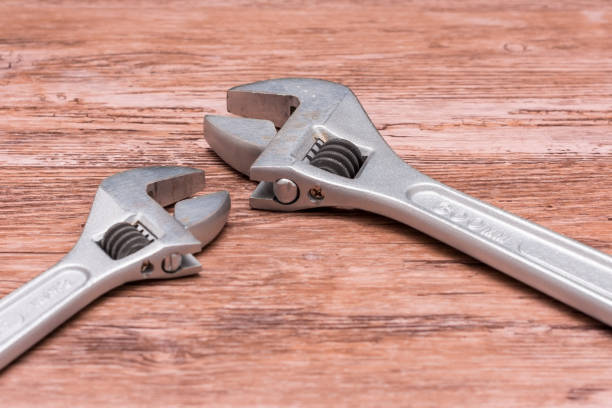 istock Two adjustable wrenches rest on a wooden surface, one large and one small. The larger wrench is positioned on the right, while the smaller one is placed on the left, highlighting the contrast in size. 2195733015