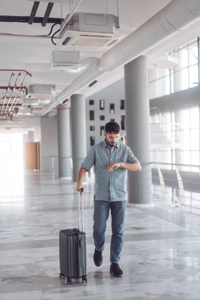 istock Young businessman checking time walking with suitcase in airport 2195743362
