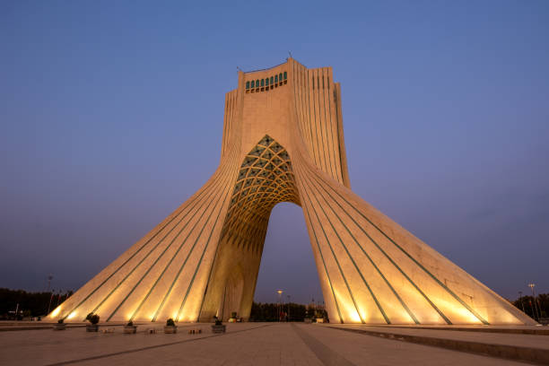 Illuminated at dusk, the azadi tower rises majestically in tehran, iran, displaying its unique architectural features against a stunning twilight sky filled with blue and purple hues