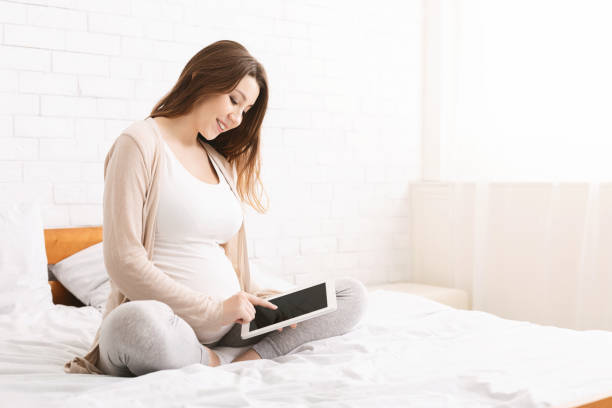 istock Pregnant Woman Using Tablet While Relaxing in Bright Bedroom During Daytime 2195746752