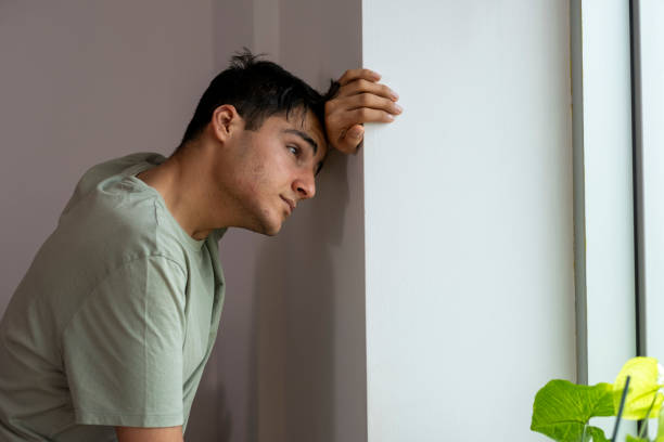 istock Young man suffering from depression leaning against wall by window 2195754116