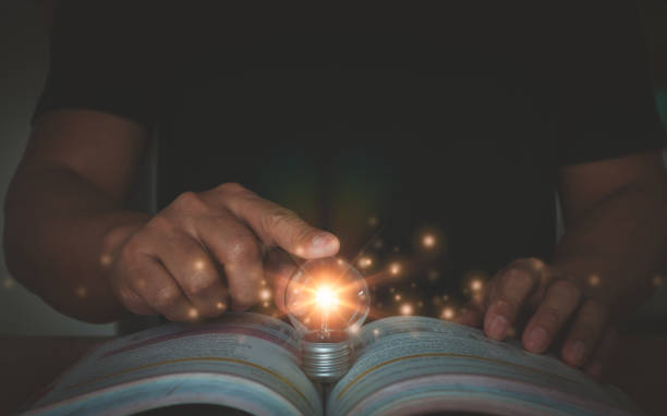 istock Self learning or education knowledge and business studying concept. Person hand touch glowing light bulb and open book. Idea of learning online class or e-learning at home. Think outside working. 2195759299