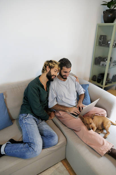 istock Gay couple using laptop with sleeping dog on sofa at home 2195768735