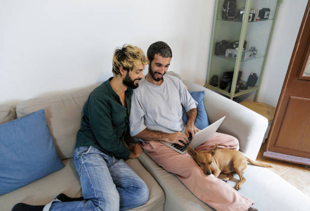 istock Gay couple using laptop with sleeping dog on sofa at home 2195768748