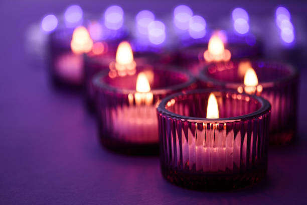 Warm candlelight in glass holders against a soft, purple background, creating a serene ambiance.