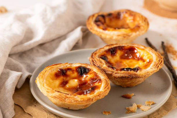 istock Three Pastel de Nata, Portuguese custard tarts, are presented on a plate with cinnamon and vanilla beans. 2195777076
