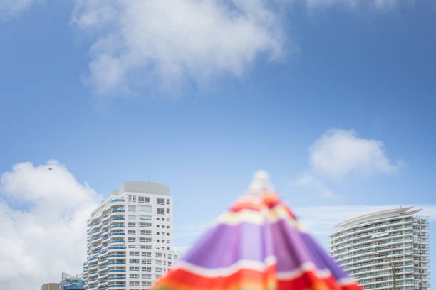 A colorful beach umbrella on the center with partial skyline view of Punta del Este city in a bright sunny day. Playa Mansa.