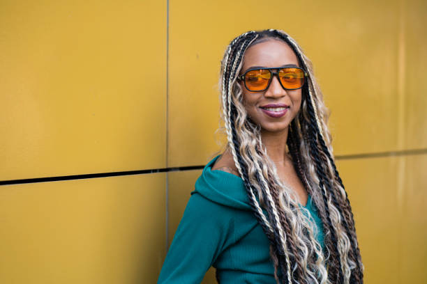 Beautiful black woman plays with her hair braids and shows her style full of energy, vitality, joy with warm colors on the street while smiling and having fun with her lifestyle