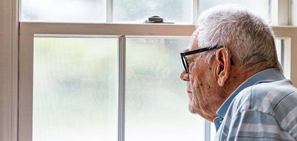 istock Elderly Man Wearing Hearing Aid Wistfully Looking Through Window 2195805730