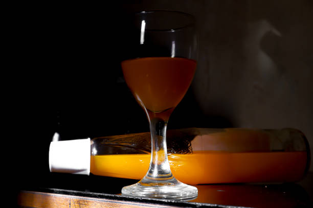 A glass and bottle of orange drink in low light