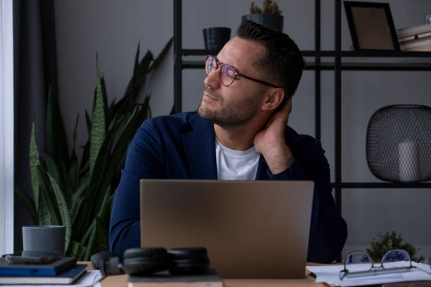 istock Businessman suffering from neck pain while working on laptop at home office 2195808927