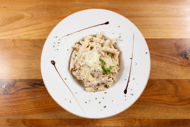 Freshly prepared creamy pasta with cheese and herbs, beautifully plated on a white dish. Perfect for illustrating culinary themes, restaurant dining, or Italian cuisine in food photography