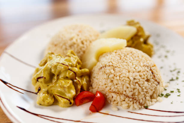 A flavorful plate of chicken curry served with rice, pineapple garnish, and fresh garnishments on a wooden table. The dish is presented beautifully, making it perfect for culinary and food-related themes