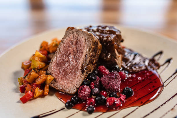 Delicious gourmet meal featuring perfectly cooked beef with vibrant roasted vegetables and tangy berry sauce, elegantly plated on a wooden table with a sophisticated artistic touch