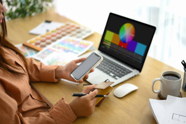 istock Female designer holding smartphone working with material and color samples at workplace 2195816992