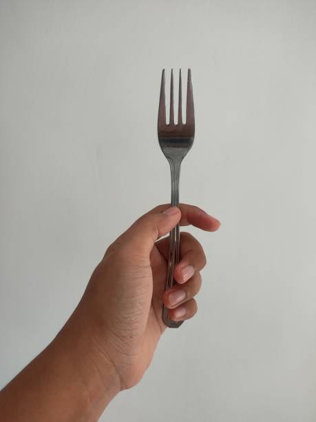 istock A hand holding a metal fork against a white background. 2195817012