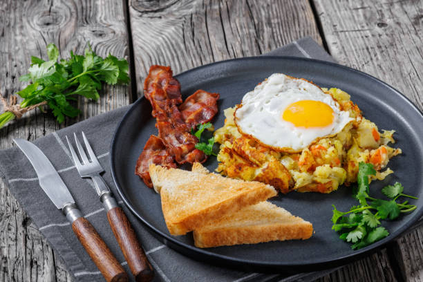 Bubble and Squeak, browned mix of leftover mashed potato and cabbage, topped with fried egg served with toast and fried bacon on a plate, on rustic wooden table, british cuisine