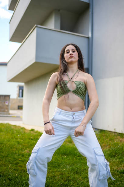 Female young caucasian dancer standing energetically performing urban dance outdoors next to buildings with garden