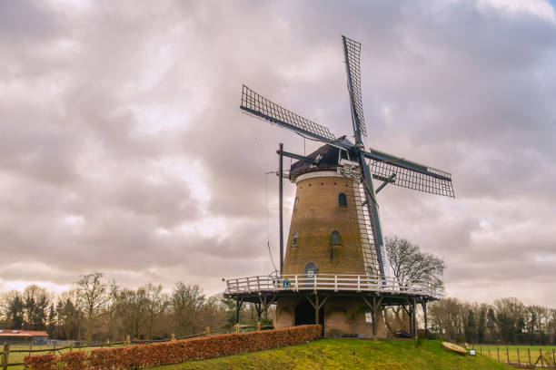 The rebuilt traditional Dutch windmill De Windhond in Soest, Netherlands, surrounded by green grass and hedges under a dramatic cloudy sky.