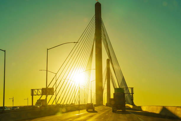 Long Beach, California - January 15, 2025: Silhouette of the Long Beach International Gateway bridge with sunlight in the background, showcasing cables and vehicles on the roadway.