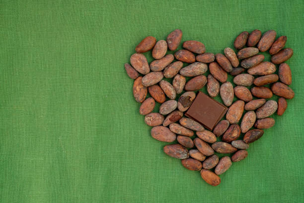 The heart is designed from cocoa beans and chocolate bars. Green linen background. Copy space.
