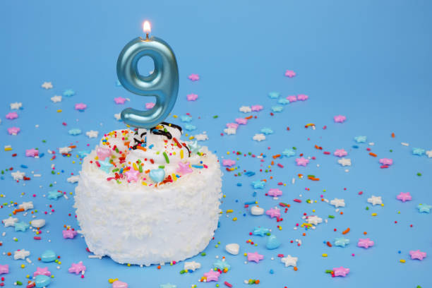 istock Coconut birthday cake on blue background with burning candle, number 9 2195842898