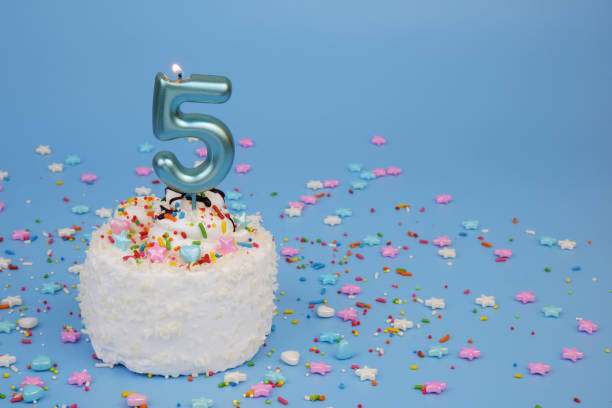 istock Coconut birthday cake on blue background with burning candle, number 5 2195842928