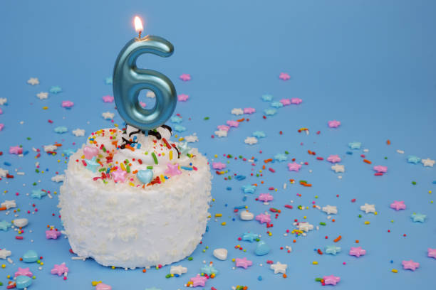 istock Coconut birthday cake on blue background with burning candle, number 6 2195842950