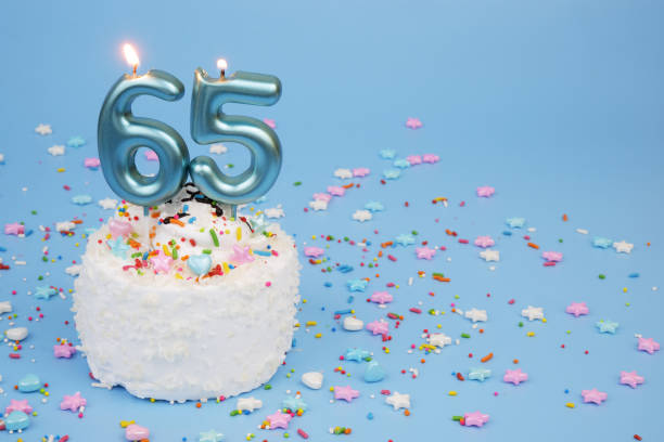 istock Coconut birthday cake on blue background with burning candles, number 65 2195843049