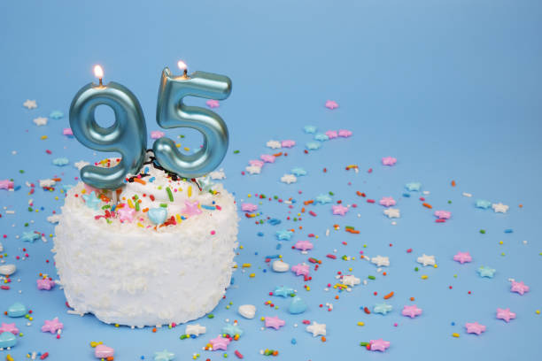 istock Coconut birthday cake on blue background with burning candles, number 95 2195843067
