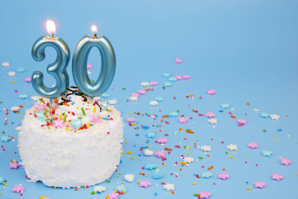 istock White coconut birthday cake on blue background with burning candles, number 30 2195843147