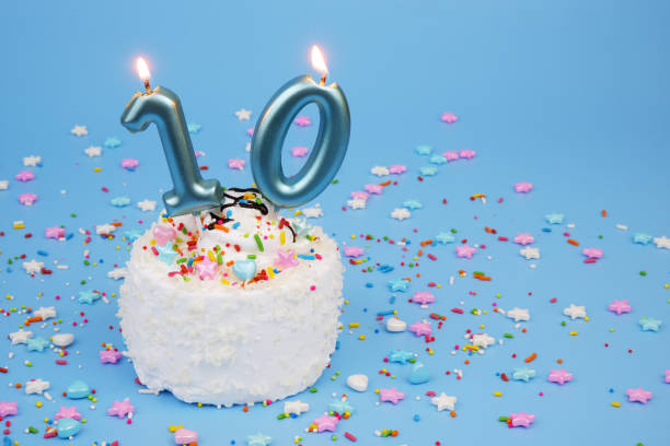 istock White coconut birthday cake on blue background with burning candles, number 10 2195843161