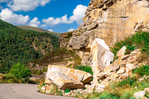 A rocky mountain side with a large rock in the middle. The rock is surrounded by smaller rocks and plants. The scene is peaceful and serene, with the mountain range in the background