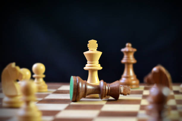 istock Brown king chess piece fallen down defeated, conquered, with the victorious elegant off white king in the centre against black background with copy space 2195844344