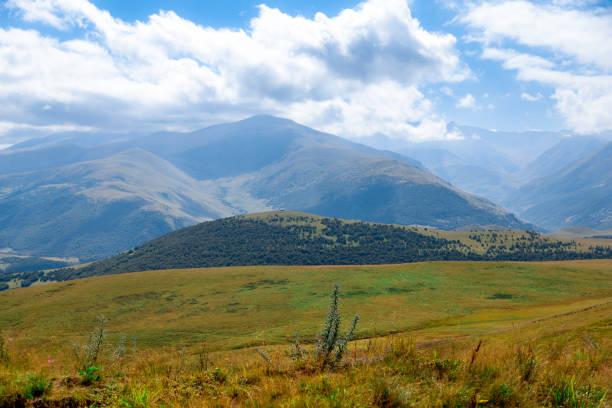 The mountains are covered in green grass and trees. The sky is cloudy and the sun is shining through the clouds