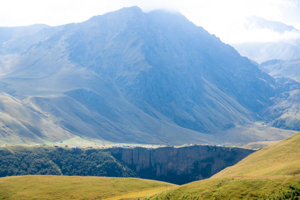 The mountains are covered in green grass and trees. The sky is clear and the sun is shining