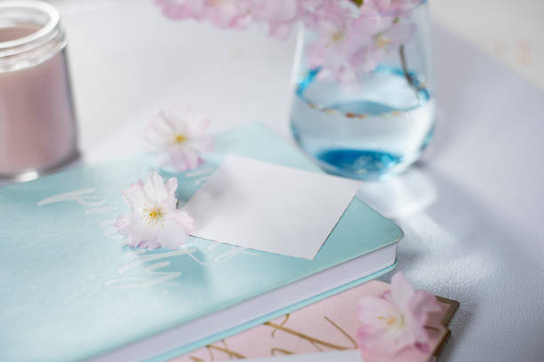 Diary, notepads, candle, delicate pink sakura flowers placed on a pastel blue table. The scene vibrates\ncalm, style and creativity, ideal for work or creative space.