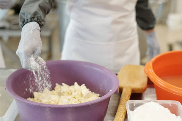 Person preparing dough in kitchen with large purple bowl, using hands covered by gloves and nearby ingredients present in various containers