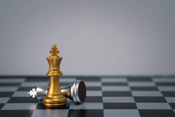 istock Gold queen chess piece standing victorious over fallen silver king piece on chessboard. Concept of strategy, victory, and leadership. 2195867422