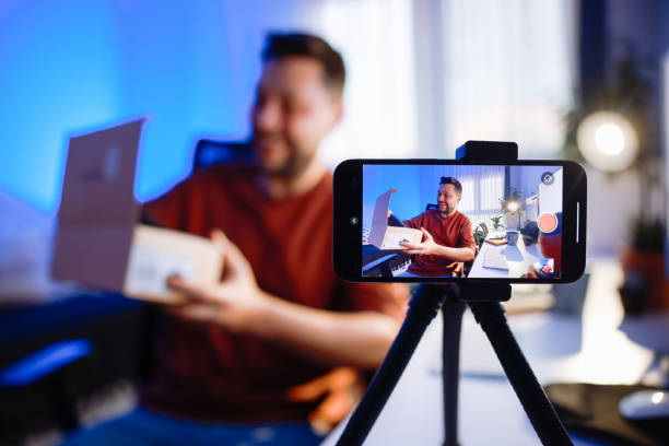 istock Male blogger unboxing parcel with tech product using smartphone on tripod, recording video content for tech blog at home 2195867797