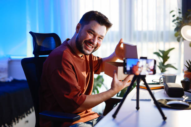 istock Male blogger unboxing parcel with tech product using smartphone on tripod, recording video content for tech blog at home 2195869413