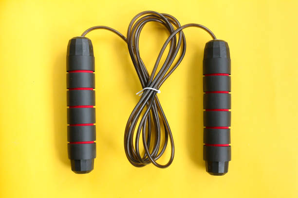 A black and red jump rope lies on a yellow background.  Perfect for fitness and exercise.