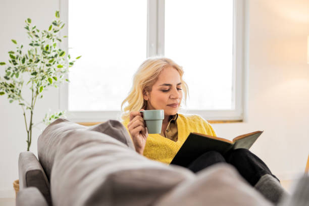 istock Woman At Home Sitting On Bed Reading Book And Drinking Coffee 2195871147