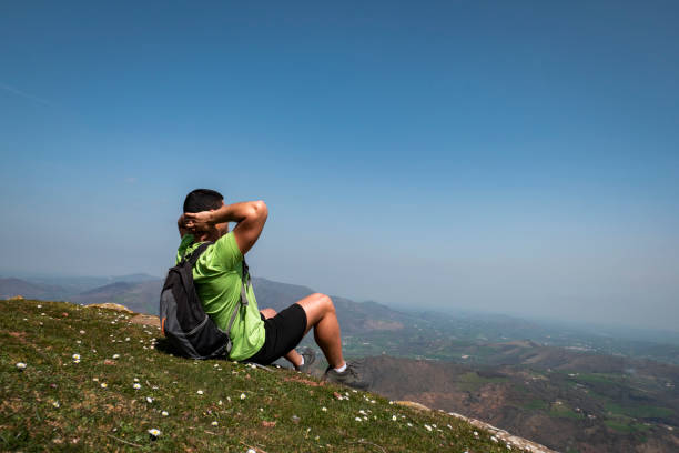Young tourist sitting relaxing while enjoying the mountains and villages in the background from the Jara mountain in Irouléguy in the Basque Country