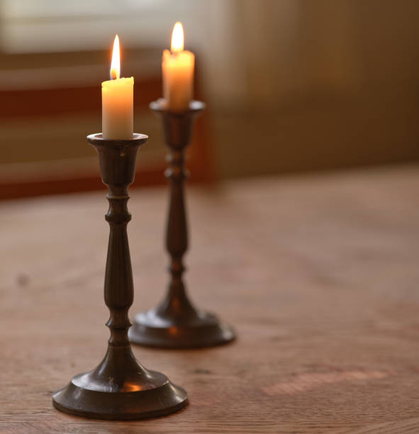 A warm and serene setting displaying two lit candles in brass candlesticks on a rustic wooden table. The soft lighting evokes a sense of tranquility, romance, and timeless elegance.