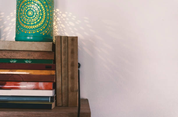 Old books and a beautiful green lamp on the shelf, in the background a white wall.