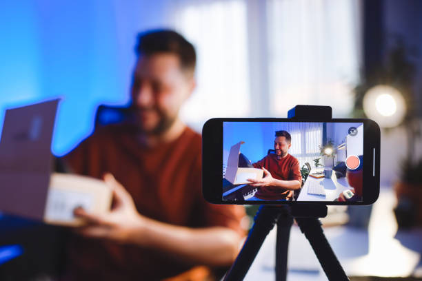 istock Male blogger unboxing parcel with tech product using smartphone on tripod, recording video content for tech blog at home 2195908109